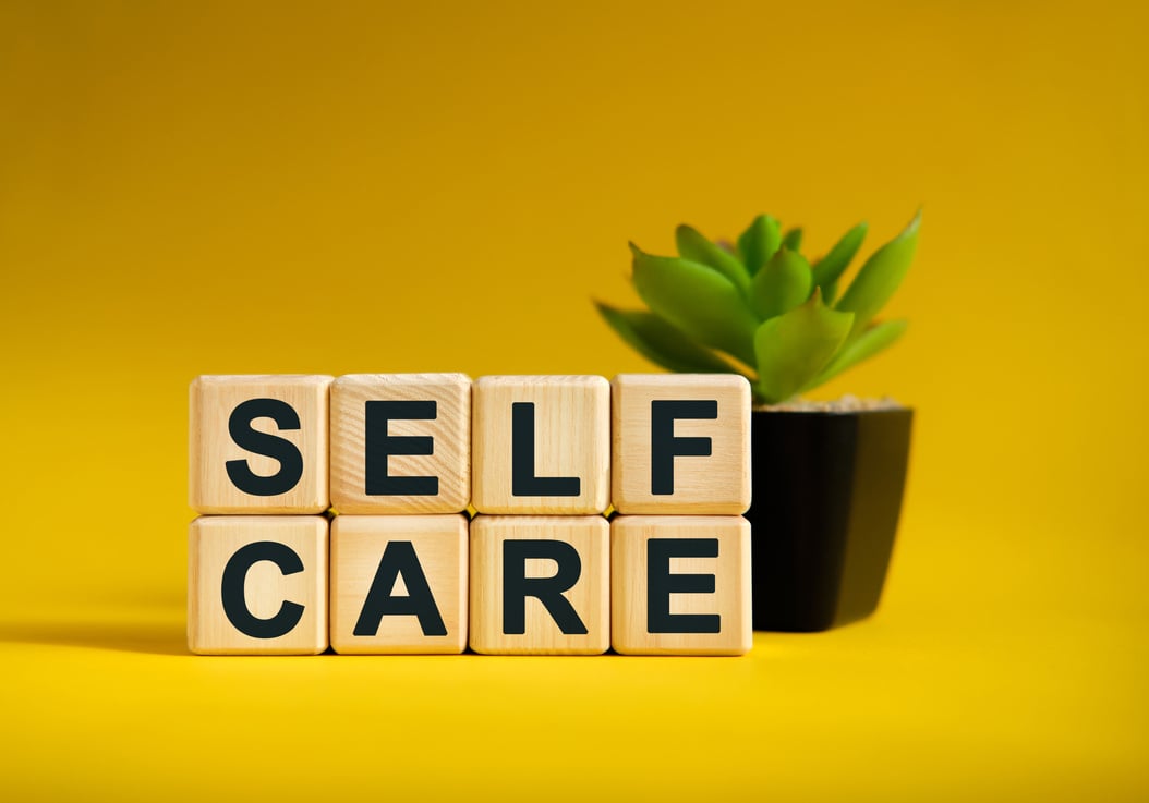 SELF CARE - text on wooden cubes, green plant in black pot on a yellow background